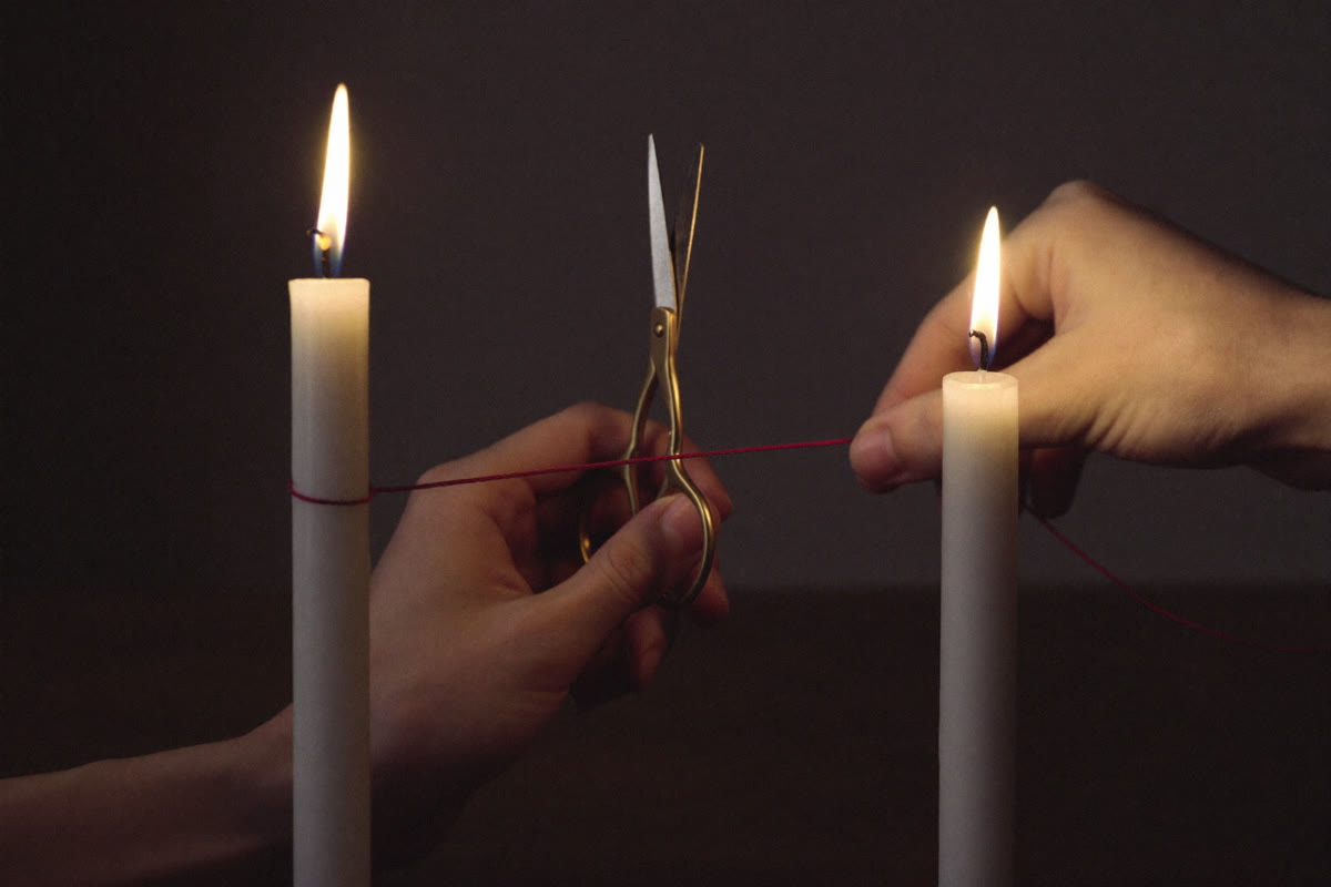Couper les liens karmiques : le geste symbolique du rituel, ciseaux et fil rouge entre deux bougies